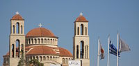 Greek and Cypriot flags being flown on flagpoles with cross finials in front of a church, Paphos.