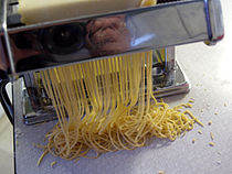 Dough being cut into noodles with a pasta machine