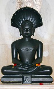 Black statue of a seated Parshvanatha, adorned with flowers