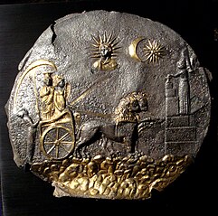 Black plate with golden decoration, depicting two figures seated in a chariot pulled by two lions facing an altar, underneath the sun, moon, and another figure.