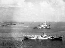 Black and white photograph of six aircraft carriers and other ships moored in rows
