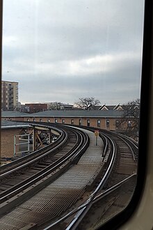 An elevated railroad track pair is seen from a train window diverging from the left.