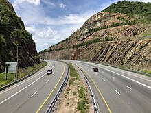 A highway passes through a cut through a mountain. The rock walls of the cut are visible above the highway.