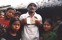 A Bhutanese man standing next to several children is depicted showing the camera his passport.