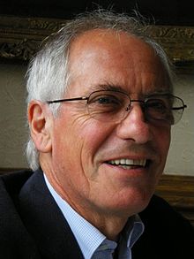 Head photograph of an older white male smiling, with short grey hair and glasses