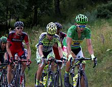 A group of cyclists riding up an incline being led by one wearing a green jersey.