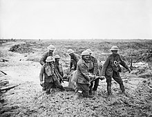 Several British soldiers, knee deep in mud, carry a wounded comrade on a stretcher.