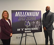 Two people stand next to a purple poster board, stating that Millennium High School is an A rated school.