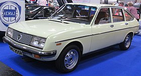 Beige four door hatch with twin headlights on a raised blue carpeted exhibition stand