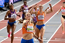 Femke Bol raising her right hand in celebration after the finish in the foreground with the other five competitors in the background