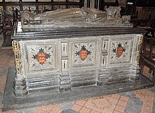 A photograph of the tomb of King John; a large carved, square, stone block supports a carved effigy of John lying down.