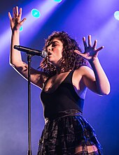 Lorde performing onstage against a purple background