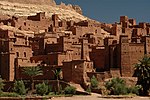 A fortified settlement with densely packed buildings and watchtowers in an arid environment