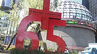 A giant sculpture that reads "Plus 65". The plus symbol has the phrase With one voice, rescue now! inscribed.