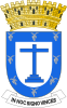 Silver leaves around the inside perimeter of a heraldic shield, in the center a blue cross and five golden towers atop