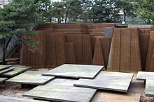 Brown-colored columns standing behind a collection of square-shaped platforms. In the background are trees and other buildings.