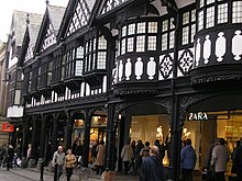 A terrace of shops with a covered walkway at ground level and timber framing above.