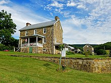 Two story stone house as seen from across a grassy yard, with a stone wall and historical marker in the foreground