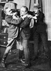 three men in an indoor setting, one attempting to throttle another