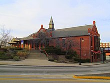 A photograph of a brick train station, which clearly shows it was designed and built a long time ago. It is well preserved.