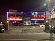 A large indoor shrimp pond building at night, with neon signs in Chinese.
