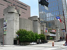 Concrete building in two sections, each with a five-sided tower on the ends. One is a curved and windowless. The other looks like a theater entrance with rounded marquee shapes and glassed entrance.