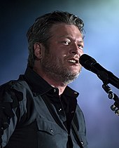 A dark-haired man wearing a dark shirt and singing into a microphone