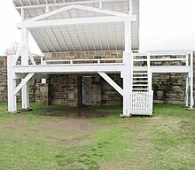 Reconstructed gallows, painted white with an open angled roof and brick wall at the rear.