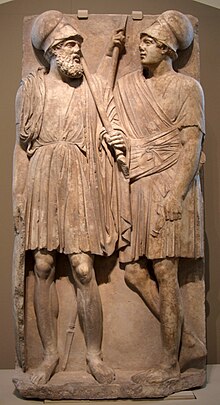 Stone slab with two men carved on it. They stand, wearing chitons.
