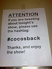 A sign indicating which Twitter hashtag to use when tweeting about the performance.