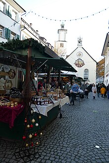 Buden und Menschen auf einem Markt mit Kopfsteinpflaster, im Hintergrund eine Kirche