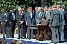 Rangel and about fourteen other men standing around a table, where President Ronald Reagan signs a bill