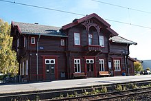 Foto eines hölzernen Bahnhofsgebäudes, mit roten Zierelementen
