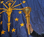 The Bicentennial Torch held up in front of a giant Indiana state flag.