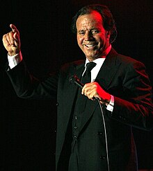 A man is facing the camera while holding a microphone with his left hand.