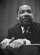 Black and white photo of Martin Luther King Jr. leaning on a lectern.
