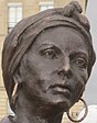 Kopf der Bronzeskulptur von Modeste Testas. Sie trägt ein zusammengeknotetes Kopftuch und große Kreolen und hat einen ernsten Gesichtsausdruck.