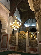 Interior of the mausoleum of Ahmad al-Tijani showing chandeliers, a decorated gate, and archways