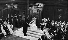 Queen Elizabeth II opening a session of the New Zealand Parliament on 12 January 1954 in the Legislative Council Chamber, Parliament House. She is accepting a vellum copy of her speech from the throne from Sir Sidney Holland (Prime Minister, 1949–1957).
