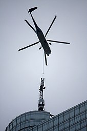 A close up view of a helicopter transporting the steeple of a building either to or from the top of the building