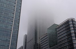 A large building heads up into the sky. Only a portion of the building is visible, as the top is engulfed in a thick fog.
