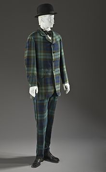 Mannequin modelling a green and blue tartan suit, with a bowler derby hat and black shoes
