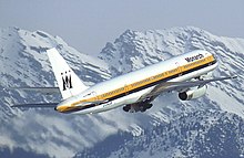 Side quarter view of aircraft at takeoff, with snow-covered mountains behind.