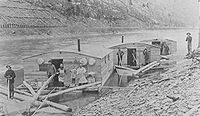 Three Arks for a log drive on Pine Creek, in Lycoming or Tioga County, Pennsylvania. The left ark was for cooking and dining, the middle ark was the sleeping quarters and the right ark was for the horses. The arks were built for just one log drive and then sold for their lumber. The line of the Jersey Shore, Pine Creek and Buffalo Railway can be seen on the eastern shore: the mountainside behind it is nearly bare of trees from clearcutting.[4]