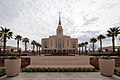 A landscape picture of the Red Cliffs Utah temple, with a sign saying it belongs to the Church of Jesus Christ of Latter-day Saints. Palm trees are seen on the side leading to the center.