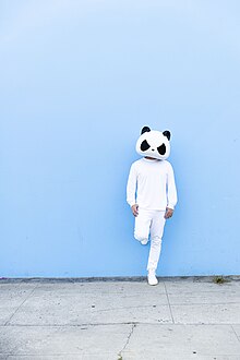 White Panda standing alone against a blue wall on a city street.