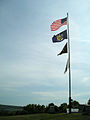 (Top down) American, New York State, Prisoner of War and New York State Office of Parks Recreation and Historic Preservation flags fly atop the hill at the battlefield