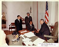 LBJ meeting with three others around the desk. The top is green.
