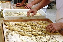 Small pieces of dough being topped with flax seeds before baking in a commercial bakery