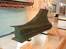 A museum exhibit of a large metal casting similar to three stacked duck bills in the front